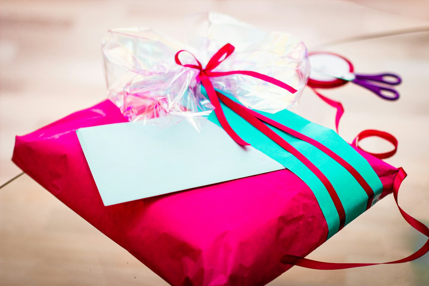 Scatola regalo fucsia con nastro turchese e fiocco rosso.